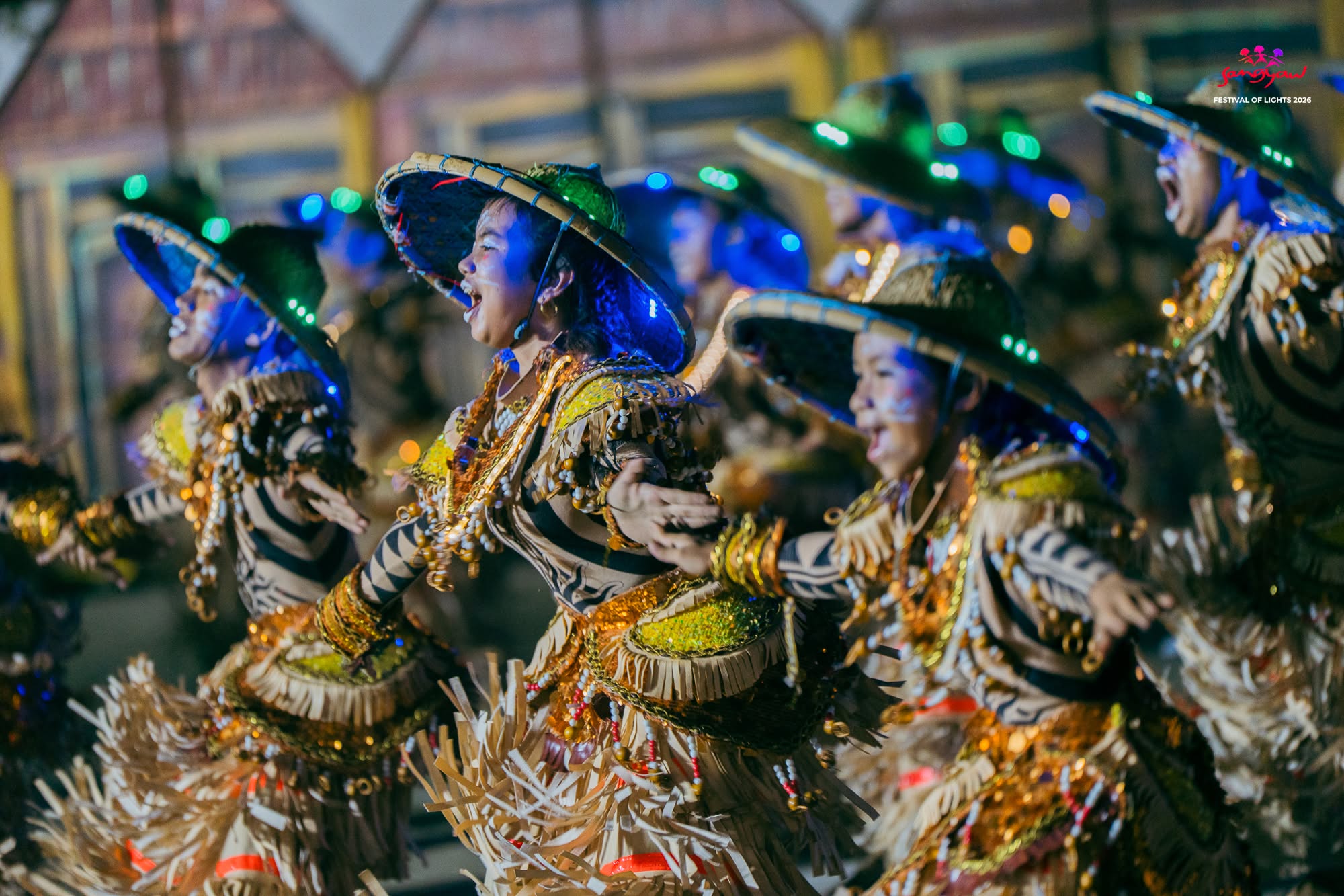 Festival dancers moving together in traditional costumes illuminated by blue and gold light